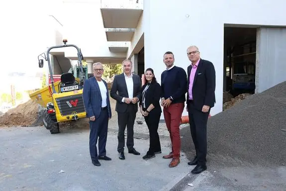 Fünf Personen stehen vor einem Bauprojekt mit gelbem Bagger in Wien